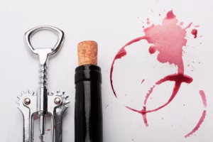 Imagem de um saca rolha, um vinho e manchas de garrafa de vinho para ilustrar a matéria como abrir vinho sem saca rolha